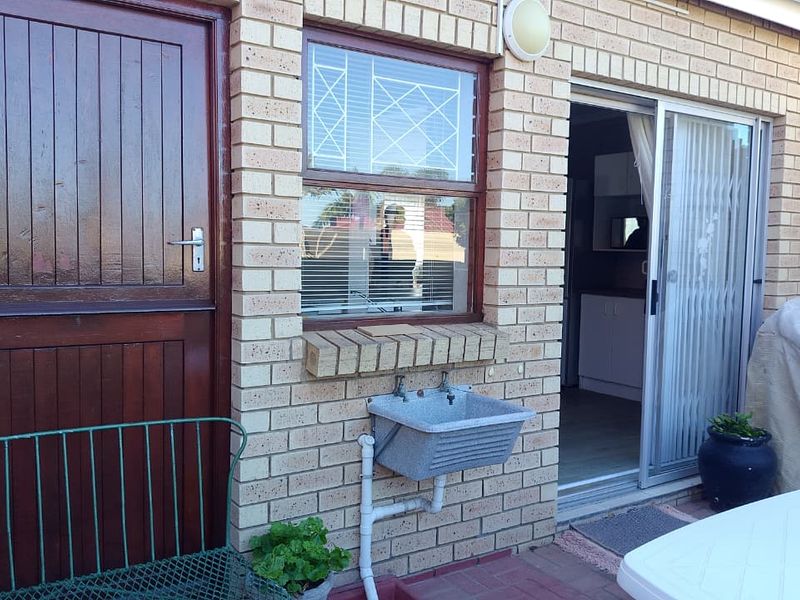 Rear exterior view of a townhouse featuring face brick walls, a timber door, a sliding glass door, and an external utility sink.
