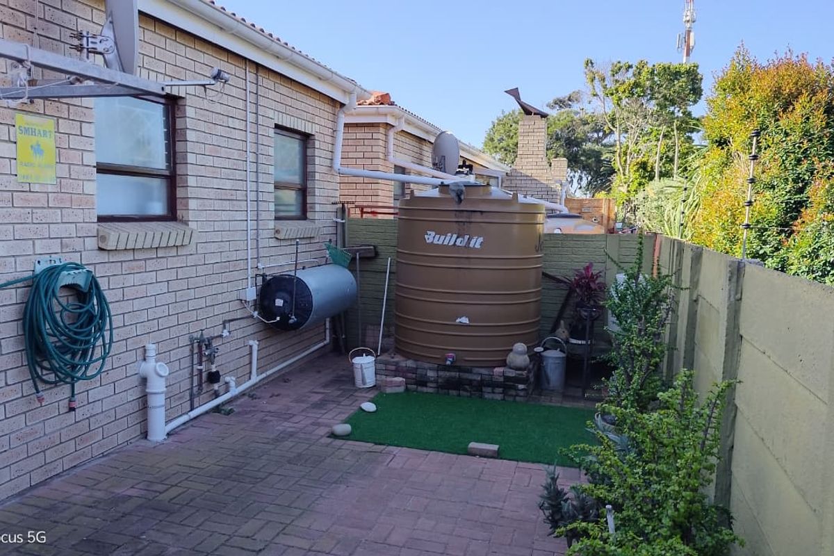 Rear courtyard area featuring a brick townhouse facade, paved flooring, a water storage tank, and perimeter security with electric fencing.