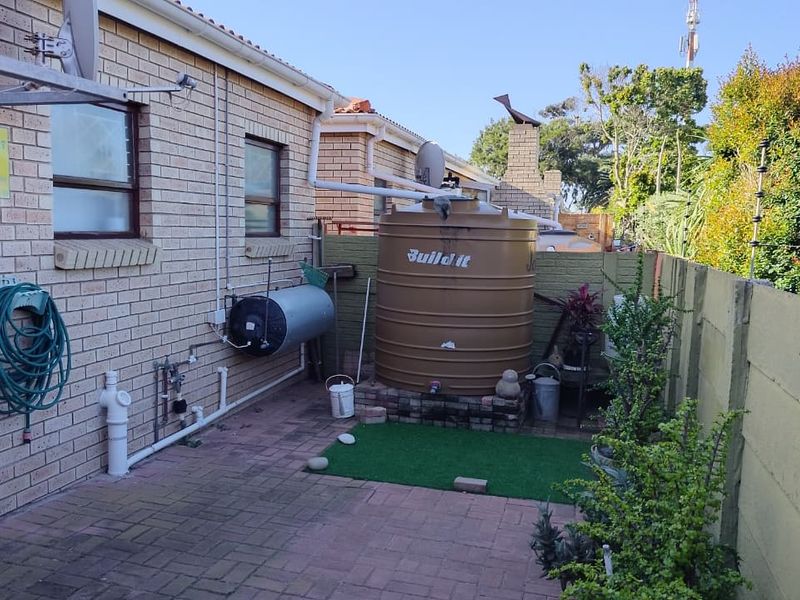 Rear courtyard area featuring a brick townhouse facade, paved flooring, a water storage tank, and perimeter security with electric fencing.