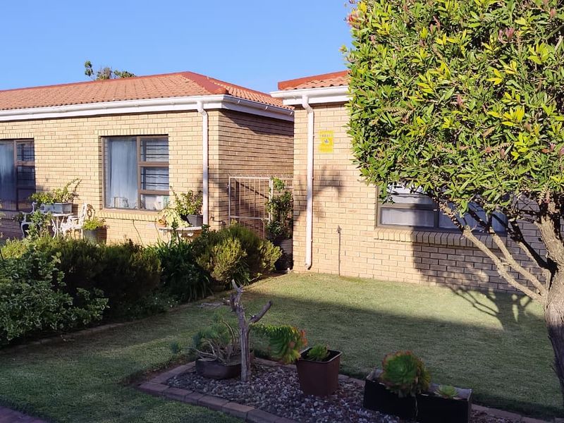 A well-maintained townhouse exterior featuring a face brick facade, tiled roof, and established garden area.