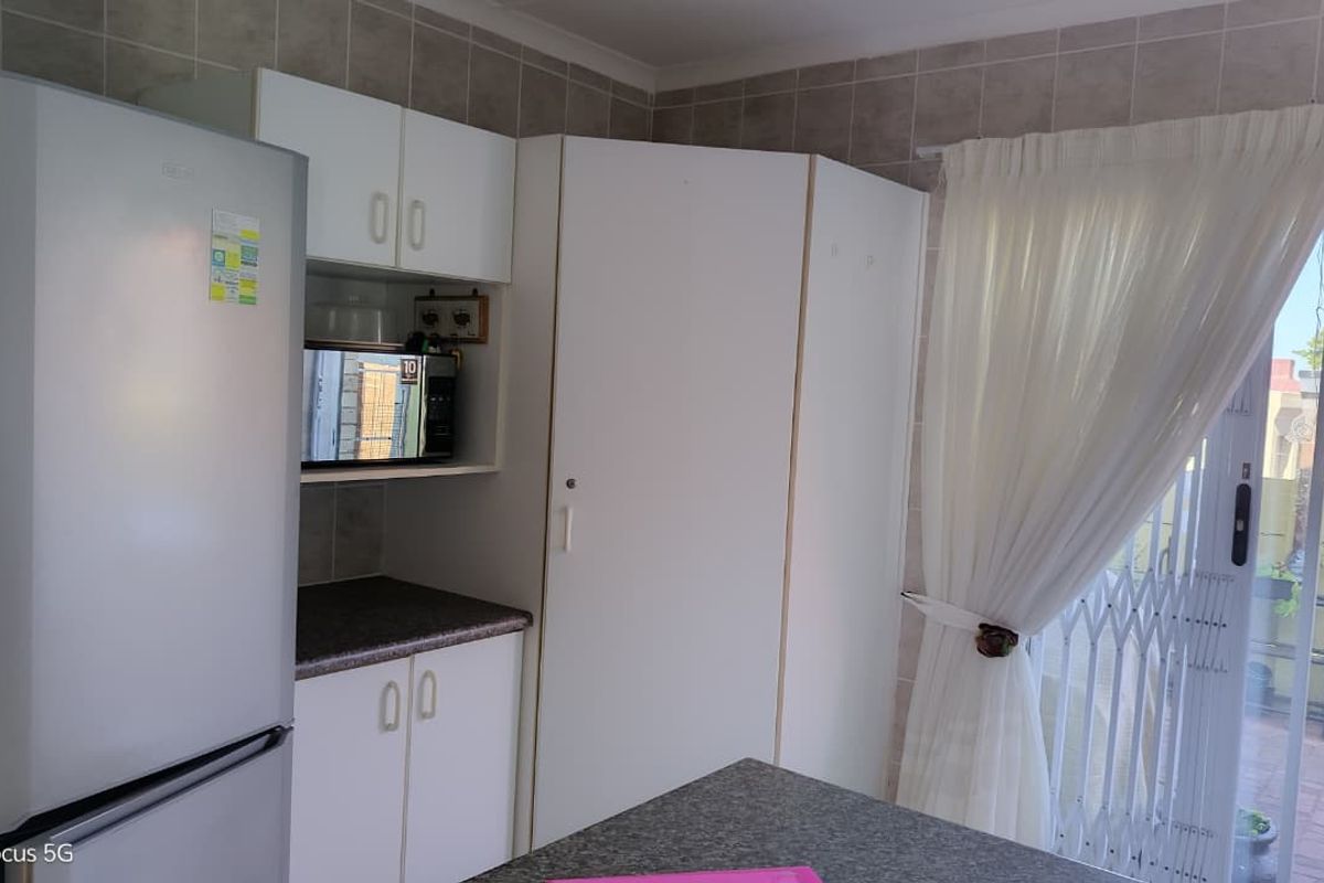 A functional kitchen area featuring white built-in cabinetry, laminate countertops, and a tiled backsplash, with direct access to an outdoor patio area.