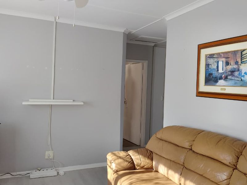 A living room area featuring neutral wall finishes, coving, and a wall-mounted shelf with visible electrical conduit.