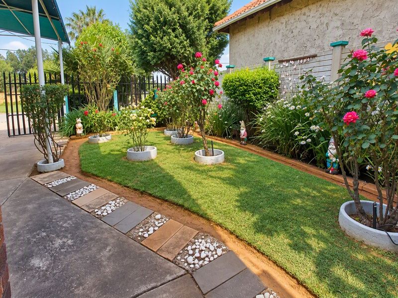 A well-maintained garden area featuring a manicured lawn, paved walkway with decorative stone accents, and established rose bushes in concrete planters.