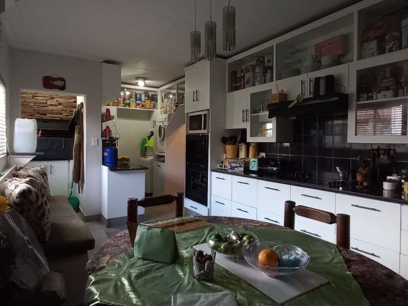 A functional kitchen featuring white cabinetry, granite countertops, built-in appliances, and a tiled backsplash, with an adjacent dining area.