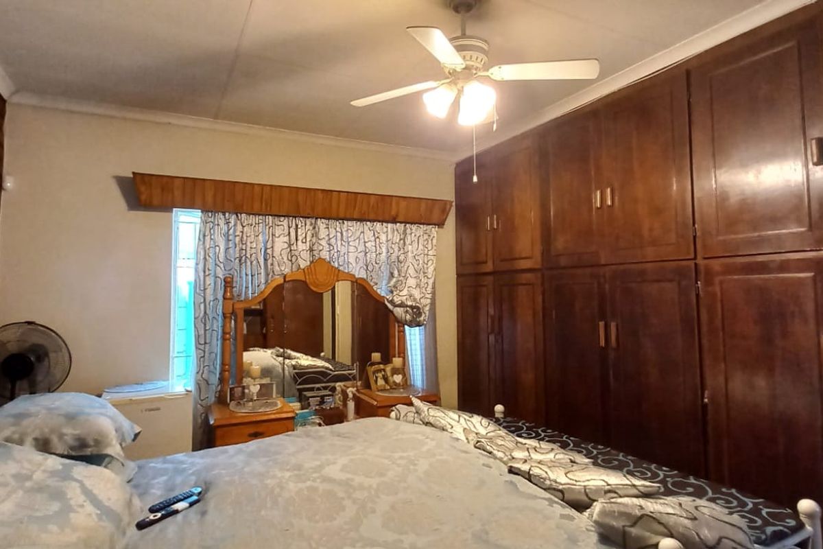 A bedroom featuring a large wall of built-in wooden cupboards, an exposed brick feature wall, and a ceiling fan.