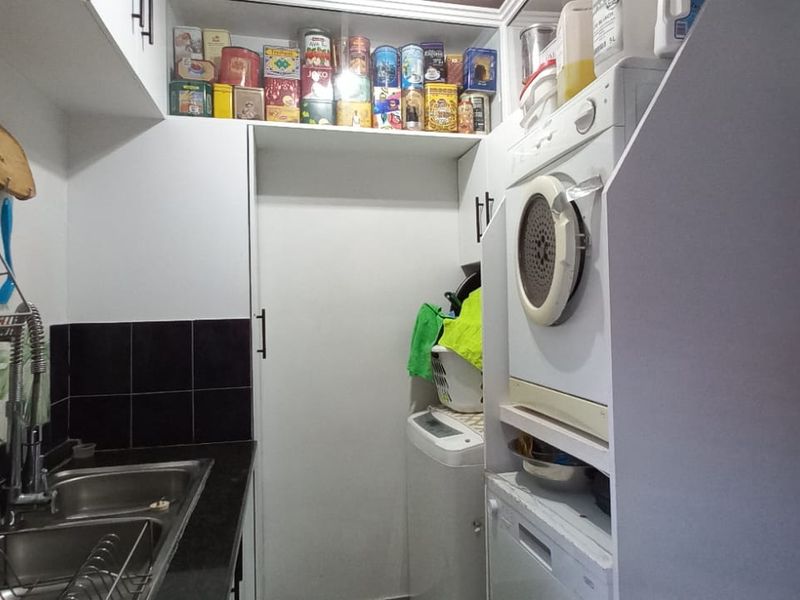 Compact scullery area featuring a double stainless steel sink, black tiled splashback, and integrated cabinetry designed for laundry and utility storage.
