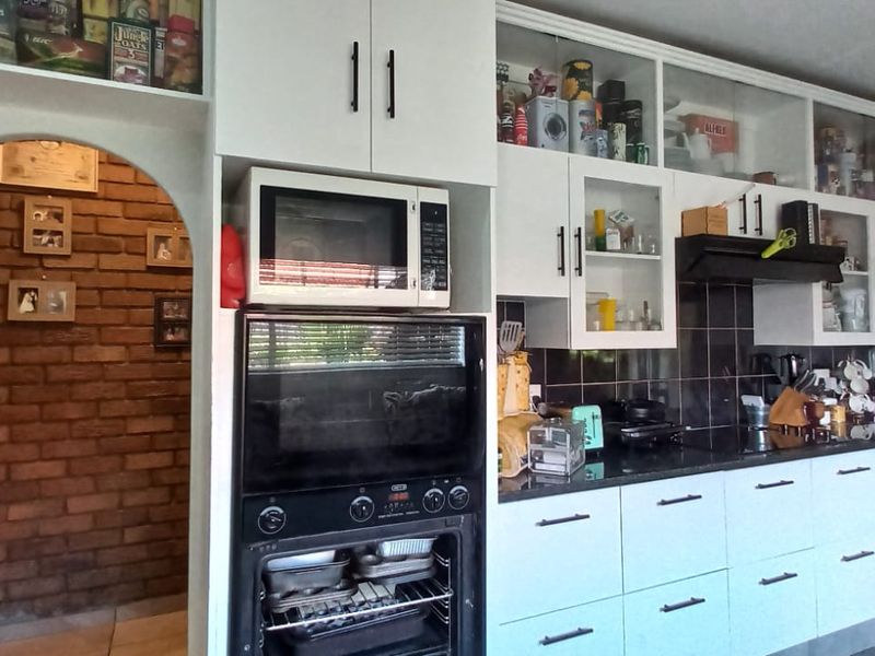 A functional kitchen featuring white cabinetry, built-in oven and microwave, dark tiled splashback, and a distinctive brick archway leading to an adjacent space.