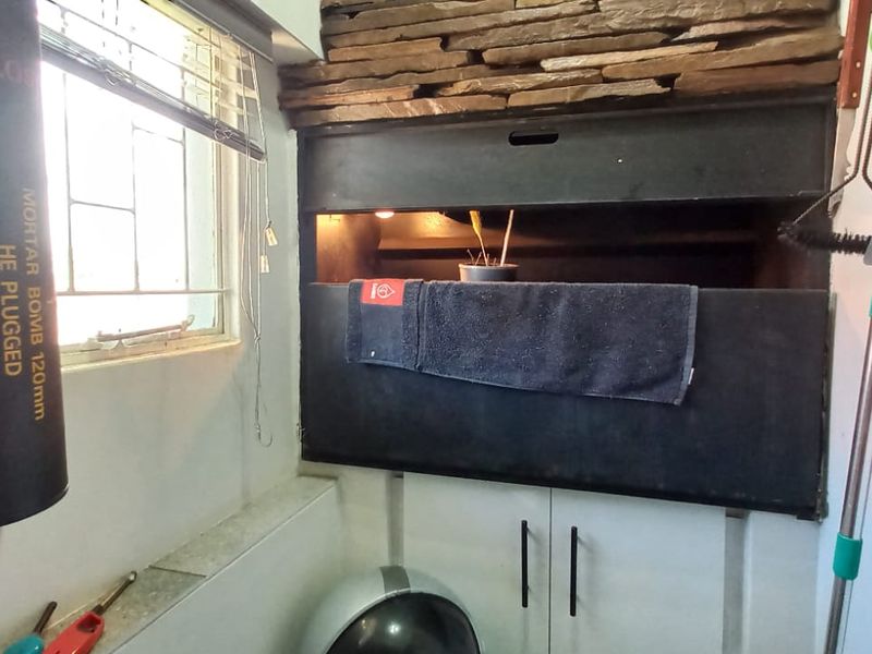 A covered patio area featuring a built-in braai with stone cladding detail and a window for natural light.