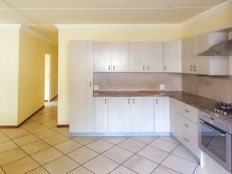 A functional kitchen featuring light-toned built-in cabinetry, stone countertops, a built-in oven, gas hob, and stainless steel extractor fan with tiled flooring.