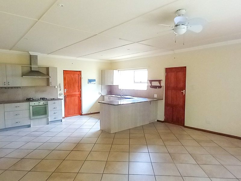 Spacious open-plan kitchen and living area featuring tiled flooring, built-in cabinetry, integrated oven and hob, and a functional kitchen island.