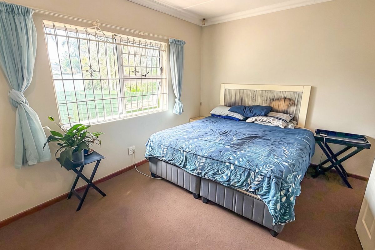 A functional bedroom featuring carpeted flooring, a window with security bars, and neutral wall finishes, offering a comfortable space for rest.
