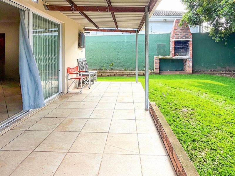Covered patio area featuring tiled flooring, a built-in brick braai, and direct access to the garden through sliding glass doors.
