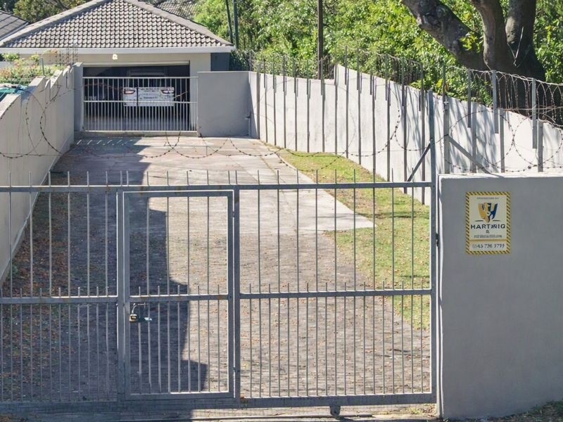A secure front entrance featuring a paved driveway, perimeter wall with razor wire, and a metal security gate leading to a garage.