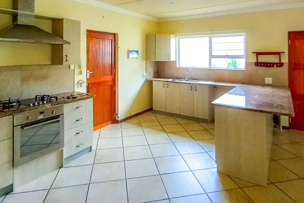 Spacious kitchen featuring built-in cabinetry, stone countertops, integrated oven, gas hob, and stainless steel extractor fan with tiled flooring throughout.