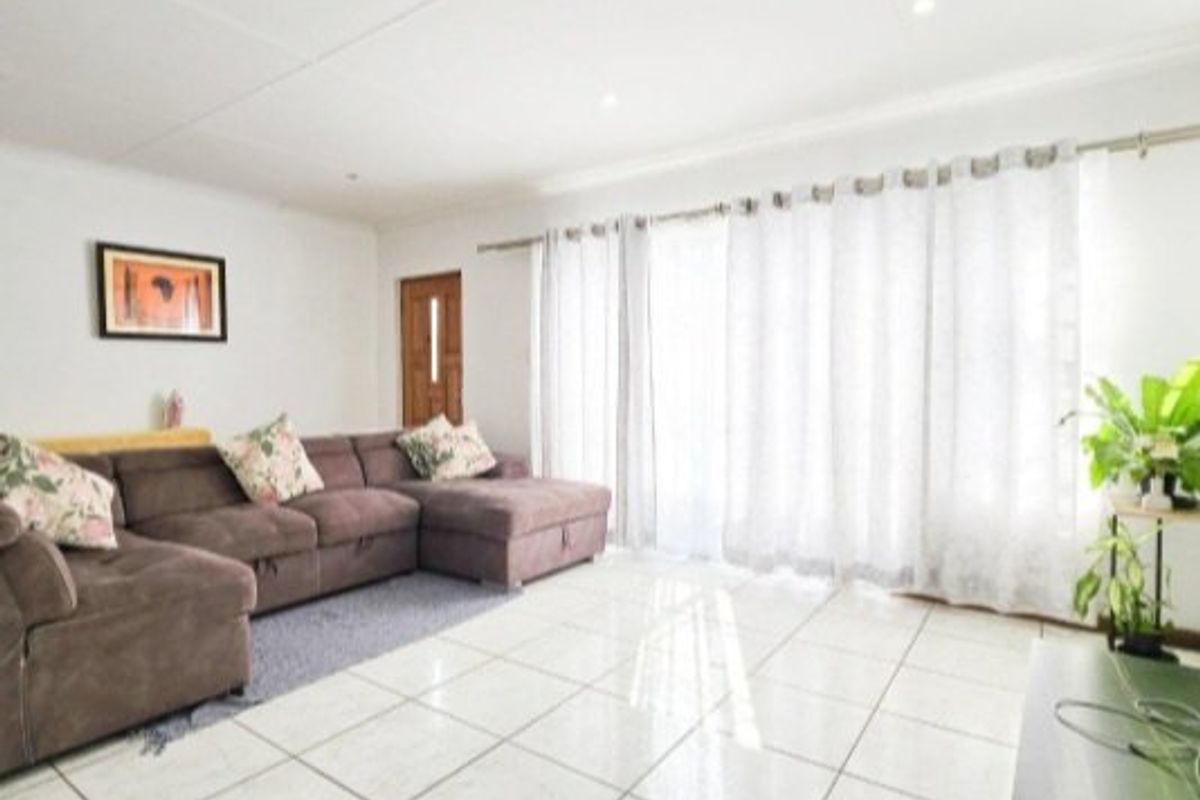 A bright and spacious living room featuring large format floor tiles, recessed lighting, and direct access to the outdoors through a sliding glass door.