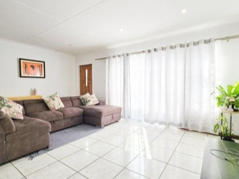 A bright and spacious living room featuring large format floor tiles, recessed lighting, and direct access to the outdoors through a sliding glass door.