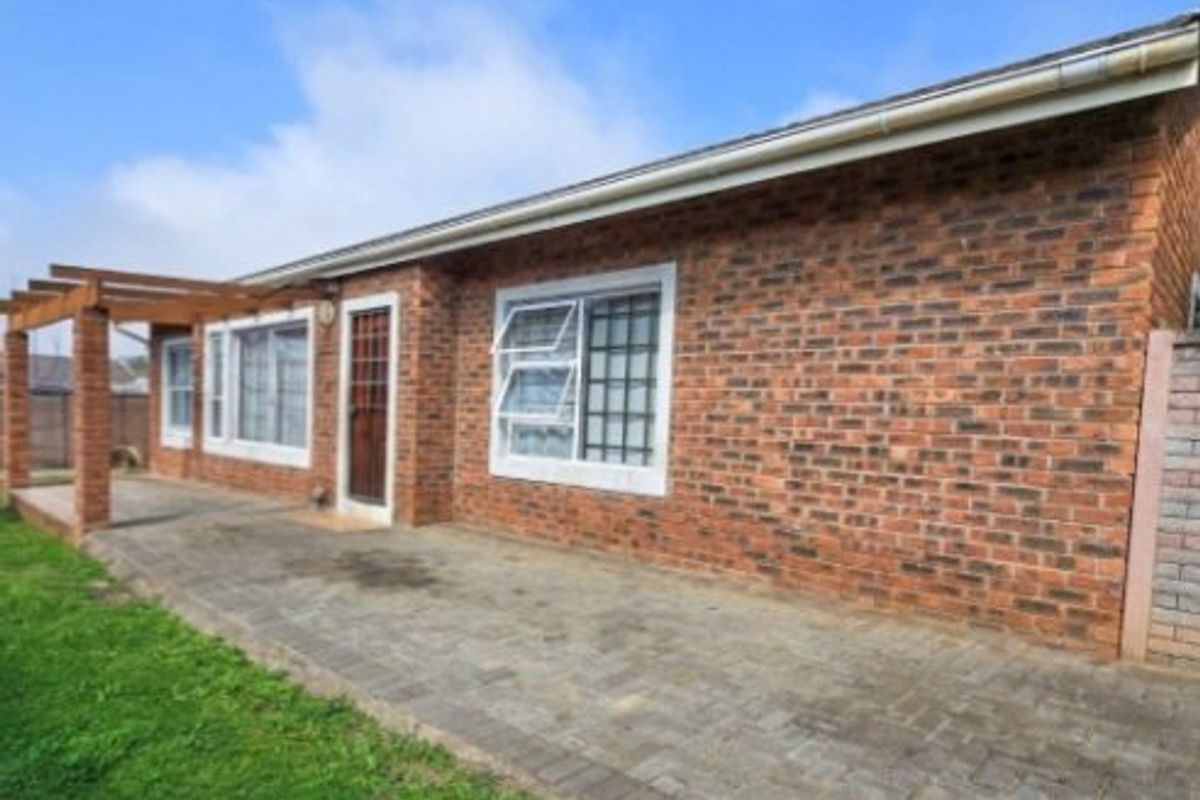 Rear exterior view of a face brick house featuring a paved patio area and a timber pergola structure.