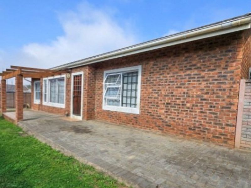 Rear exterior view of a face brick house featuring a paved patio area and a timber pergola structure.