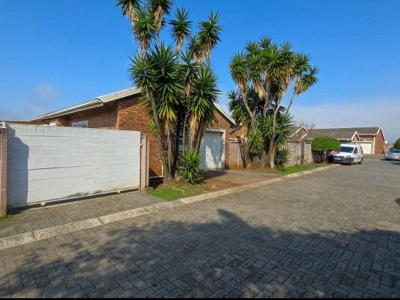 Front exterior view of a brick house featuring a paved driveway, boundary wall, and garage access.