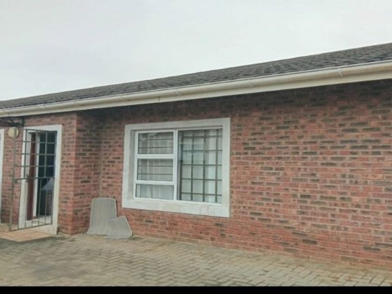 A front exterior view of a face brick house featuring a tiled roof, paved driveway, and security gates on the entrance and windows.