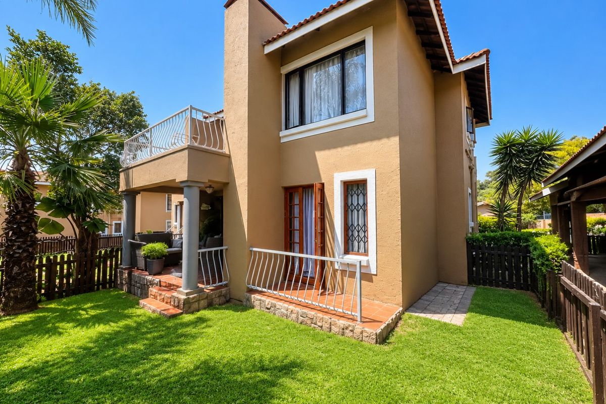 Rear view of the apartment featuring a private garden, a ground-floor tiled patio, and an upper-level balcony with metal railings.