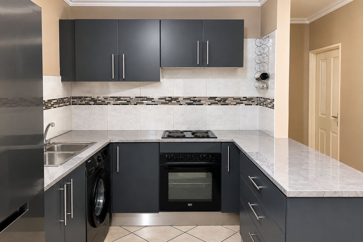 Modern kitchen featuring dark grey cabinetry, stone countertops, integrated oven and hob, and a tiled backsplash with decorative inlay.
