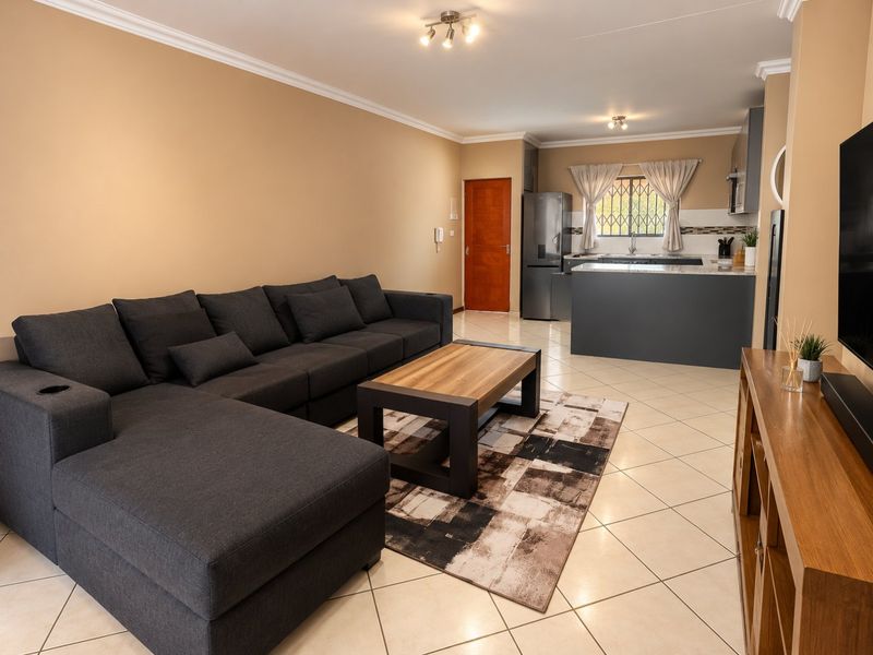 An open-plan living area featuring a modern kitchen with a central island, tiled flooring, and neutral wall finishes.