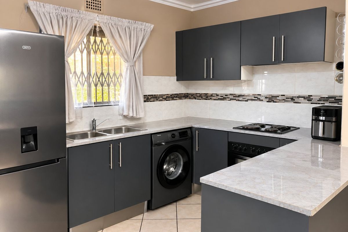 Modern kitchen featuring dark grey cabinetry, stone-look countertops, built-in oven and hob, and integrated laundry plumbing.