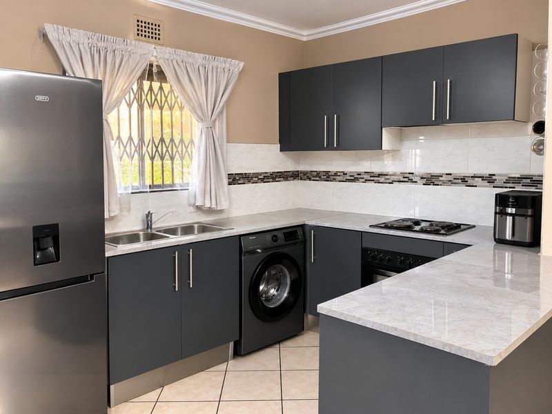Modern kitchen featuring dark grey cabinetry, stone-look countertops, built-in oven and hob, and integrated laundry plumbing.
