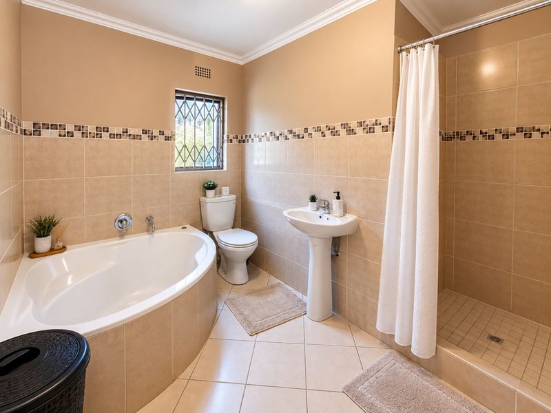 A well-maintained bathroom featuring a corner bathtub, separate shower enclosure, pedestal basin, and neutral wall tiling with decorative accents.