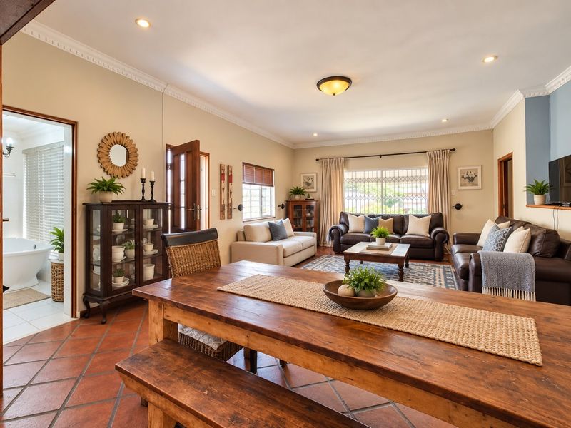 Spacious open-plan living and dining area featuring terracotta floor tiles, decorative ceiling cornices, and recessed lighting, with an adjacent view into a bathroom.