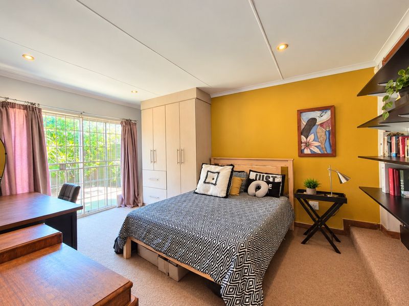 A well-lit bedroom featuring built-in cupboards, carpeted flooring, and a sliding glass door providing access to the exterior.