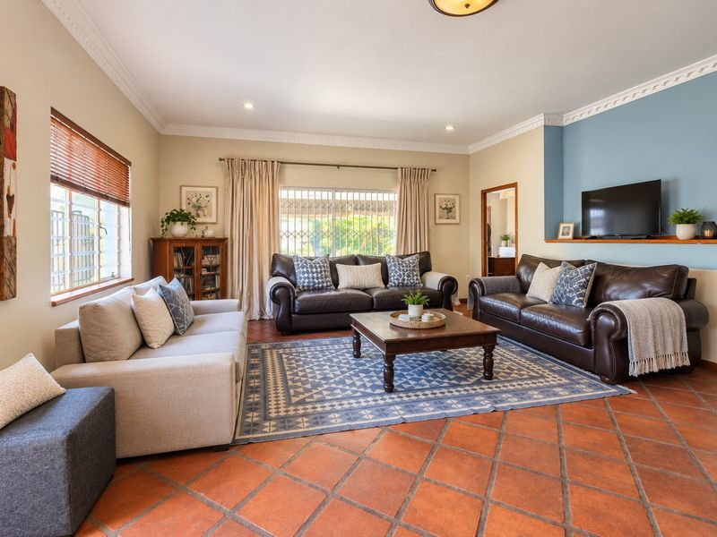 Spacious living room featuring terracotta tile flooring, crown molding, recessed lighting, and a blue accent wall with a built-in display shelf.