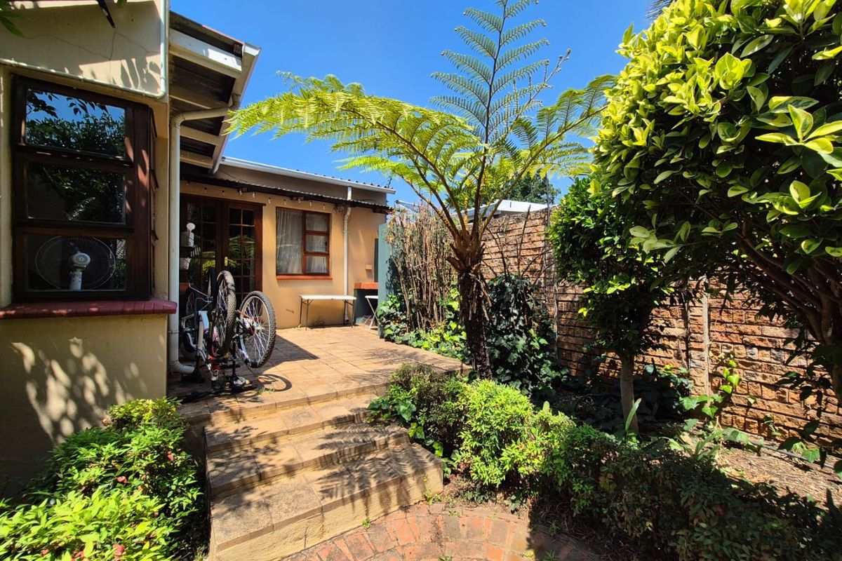 A private rear garden area featuring a paved patio, established landscaping, and brick boundary walls, providing a quiet outdoor space.