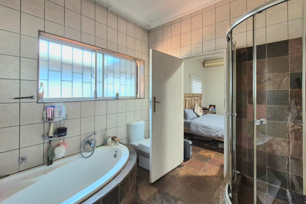 A functional bathroom featuring a built-in bathtub, corner shower enclosure, and toilet, with tiled walls and flooring throughout.