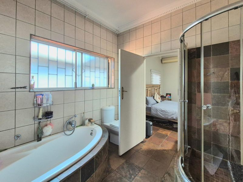 A functional bathroom featuring a built-in bathtub, corner shower enclosure, and toilet, with tiled walls and flooring throughout.