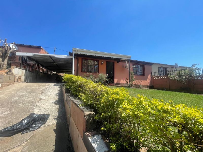 Front exterior view of the house featuring a concrete driveway, attached carport, landscaped garden, and perimeter security fencing.