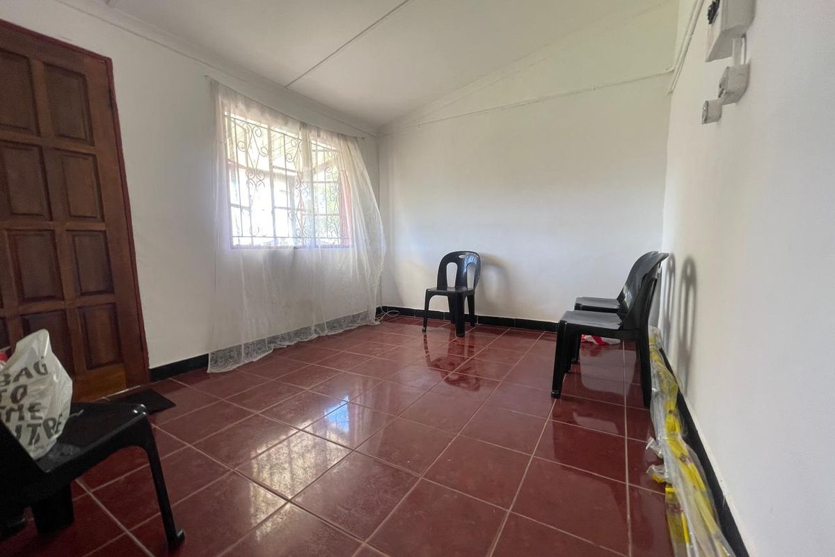 A sparsely furnished living area featuring red tiled flooring, a timber door, and security-fitted windows, presenting a blank canvas for interior design updates.