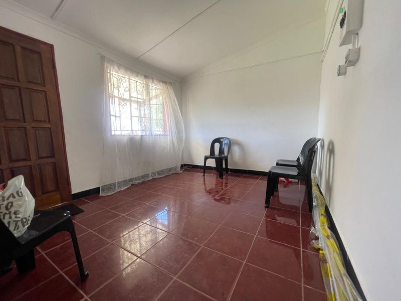 A sparsely furnished living area featuring red tiled flooring, a timber door, and security-fitted windows, presenting a blank canvas for interior design updates.