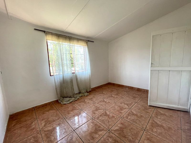 An empty bedroom featuring tiled flooring, a window with security bars, and a standard interior door.
