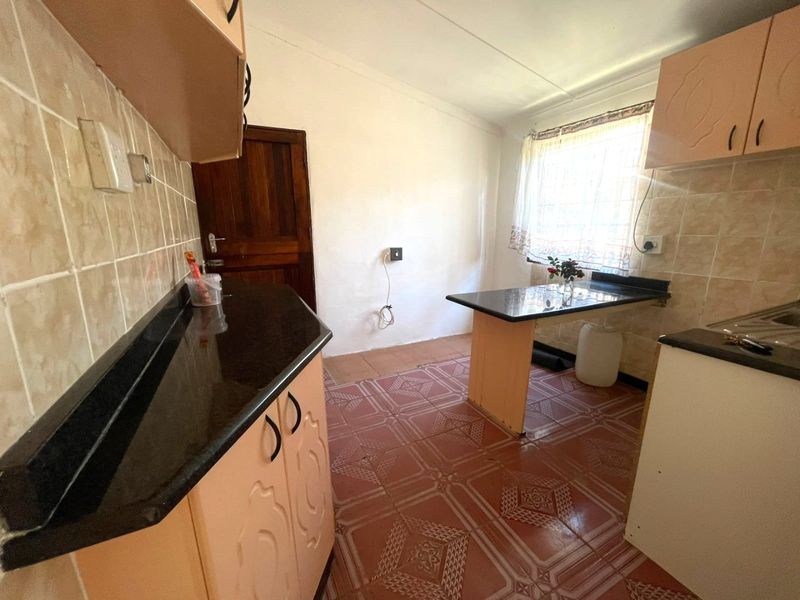 A functional kitchen featuring built-in cabinetry, granite countertops, and tiled flooring, offering a blank canvas for potential modern updates and renovation.