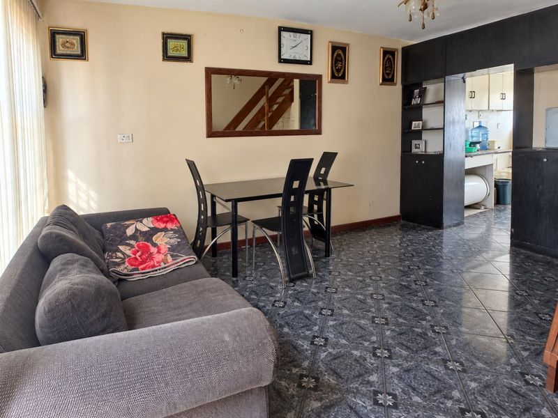 Open plan living and dining area featuring tiled flooring and a built-in shelving unit, with an adjacent view into the kitchen space.
