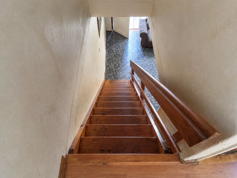 A view looking down a wooden staircase leading to a tiled lower level area with visible wear on the walls and stair treads.