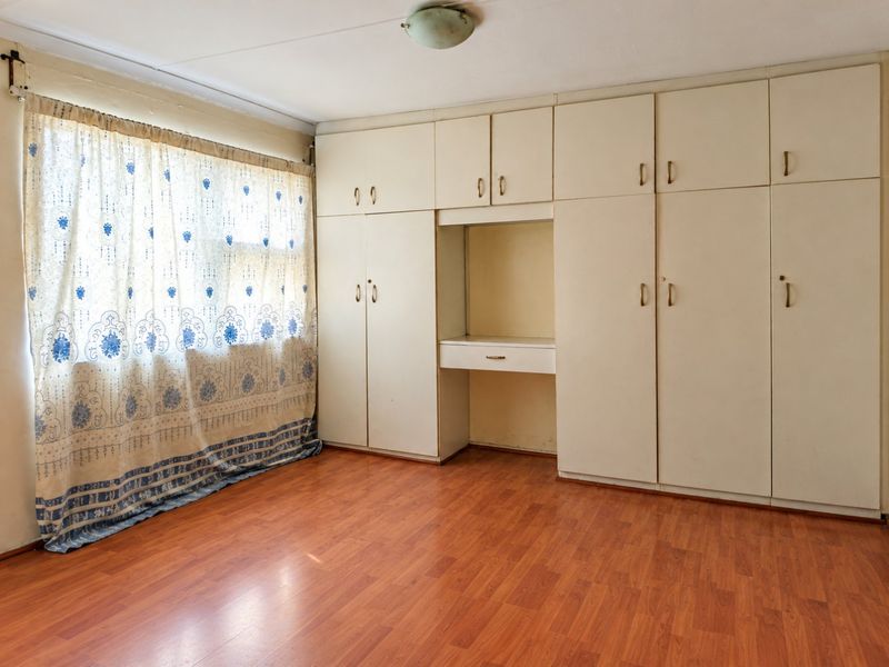A spacious bedroom featuring extensive built-in cupboards with an integrated vanity area and warm-toned laminate flooring.