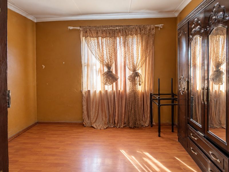 A bedroom featuring laminate flooring and coved ceilings, currently requiring cosmetic updates to the wall finishes.