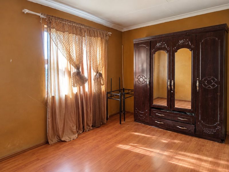 A bedroom featuring laminate flooring and coved ceilings, currently requiring cosmetic updates to the wall finishes.