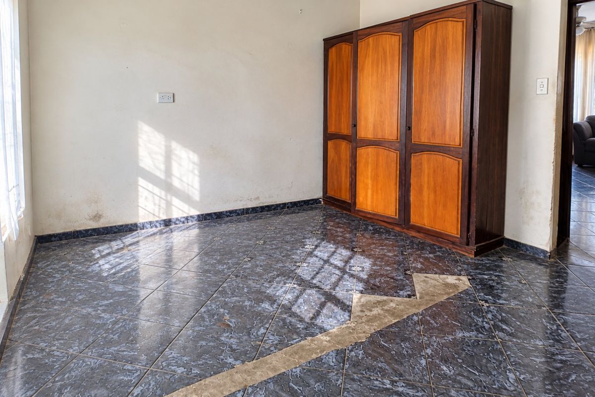 A bedroom featuring dark tiled flooring, a built-in wooden wardrobe, and visible wall and floor maintenance requirements.