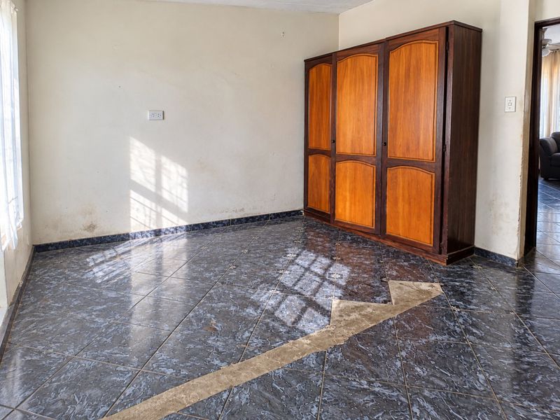 A bedroom featuring dark tiled flooring, a built-in wooden wardrobe, and visible wall and floor maintenance requirements.