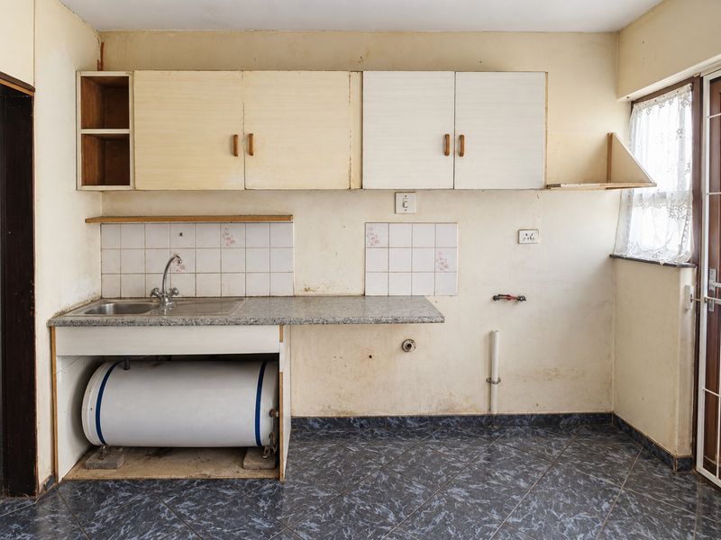 A dated kitchen area featuring basic laminate cabinetry, a stainless steel sink, and tiled flooring, requiring significant renovation and cosmetic updates.