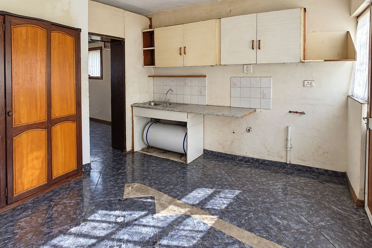 A dated kitchen area featuring basic cabinetry, a sink, and tiled flooring, requiring significant renovation and cosmetic updates to modernize the space.